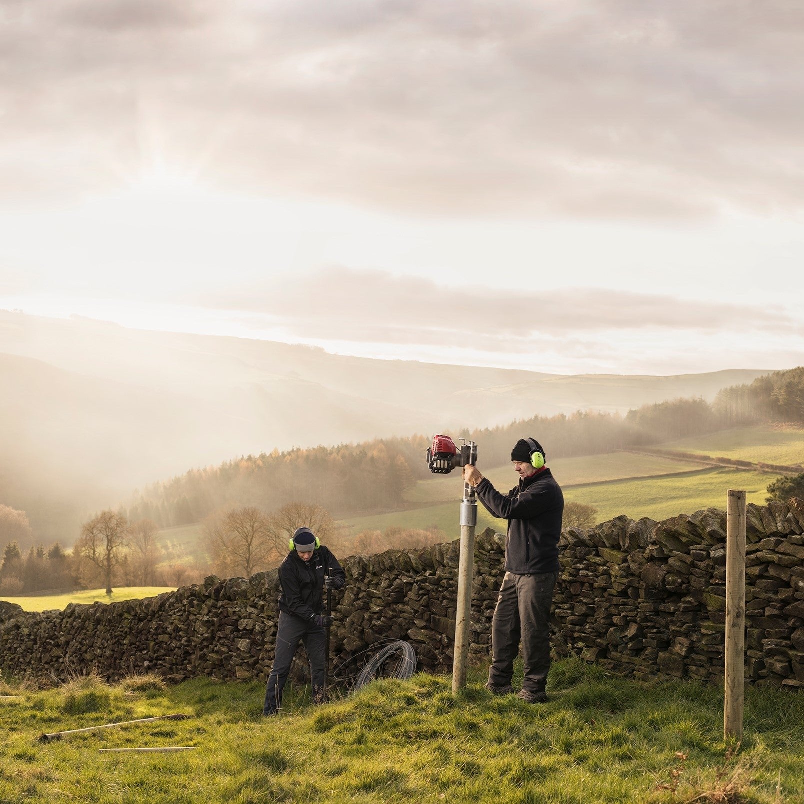 Farm contractors installing a 4" timber fence along a stone wall